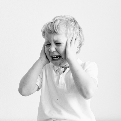 a young boy crying and covering his ears.