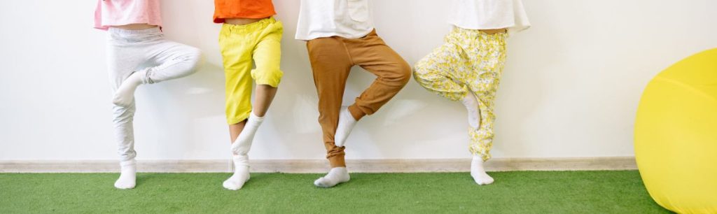 children lined up against a wall, wearing colourful clothes and balancing on one leg, doing occupational therapy