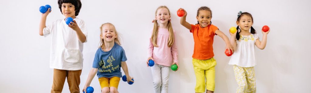 a picture of children lined up against a wall and throwing colourful plastic balls at the camera.