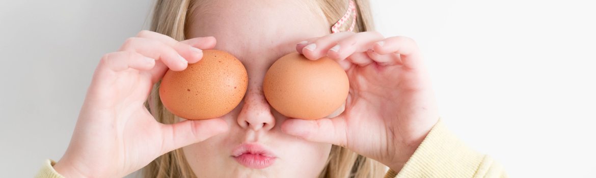 a girl holding two eggs in their shells up, and placing them over her eyes.