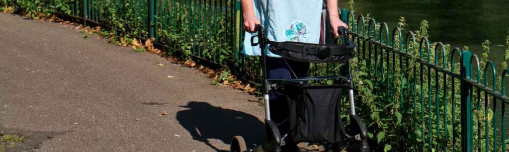lady walking along a path with a mobility aid, a four wheeled walker. Adult Occupational Therapy Services.
