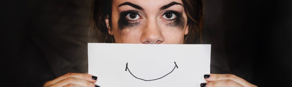 photo-of-a-lady-with-smudged-makeup-looking-sad-holding-up-a-piece-of-paper-with-a-smiley-mouth-drawn-on-it.