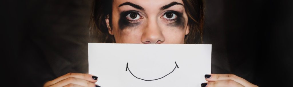 photo-of-a-lady-with-smudged-makeup-looking-sad-holding-up-a-piece-of-paper-with-a-smiley-mouth-drawn-on-it. occupational therapy cornwall