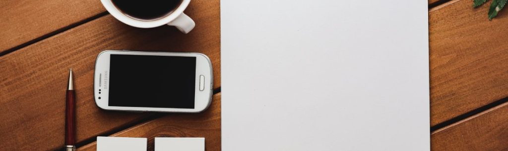 picture to indicate writing a report for a case manager photo of a mug of black coffee, a mobile phone and a pad of paper on a wooden board on a white background. Case Managers