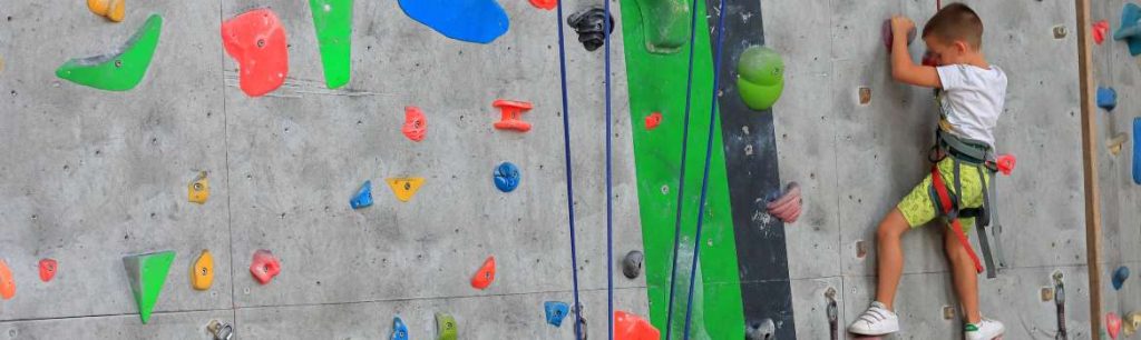 a boy climbing up a climbing wall wearing a harness