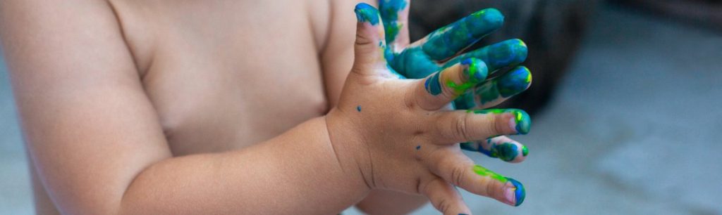 a baby with blue and green paint all over their hands. SPD, sensory play, water play, sand play, messy play.