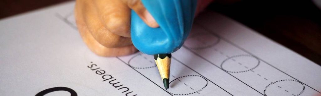 child learning to write and hold a pencil by using a pencil grip. Improving Handwriting Skills: Challenges and Tips
