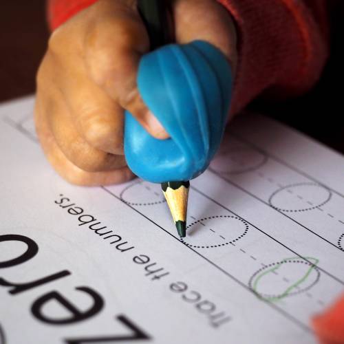 child learning to write and hold a pencil by using a pencil grip