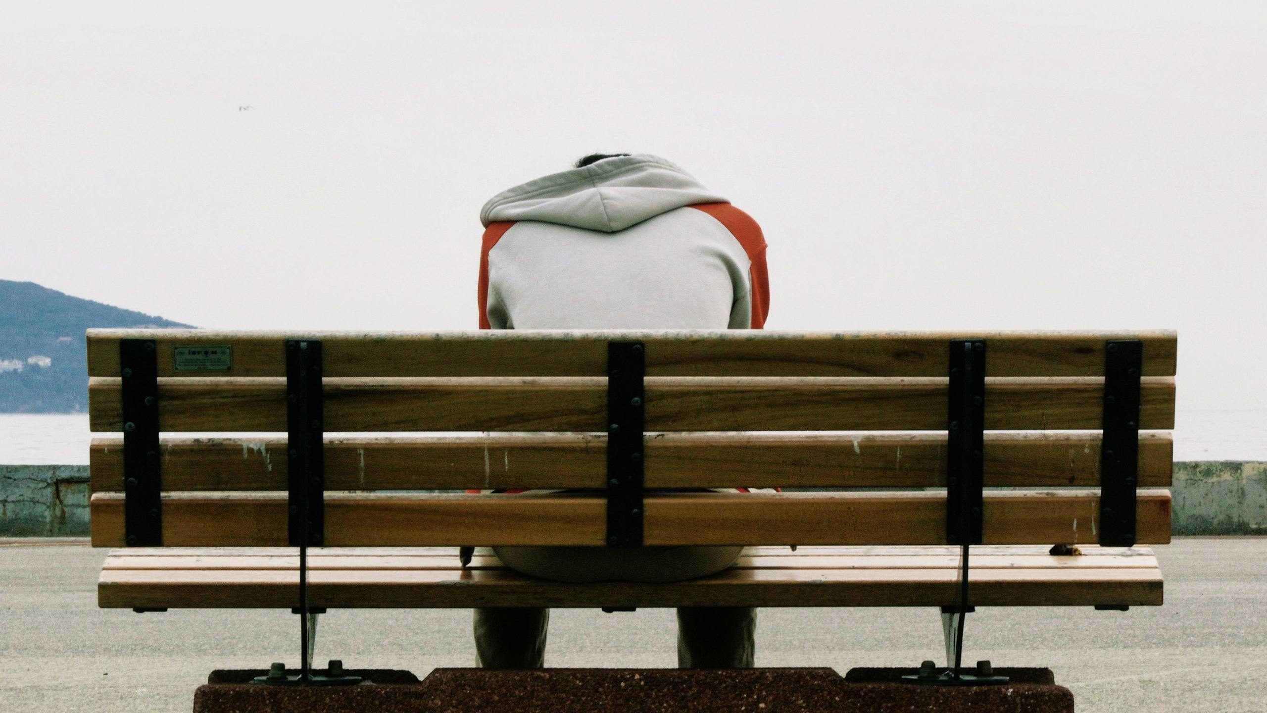 Person Wearing Grey and Orange Hoodie Sitting on Brown Wooden Park Bench during Daytime. Fighting Loneliness Through Connection Strategies.