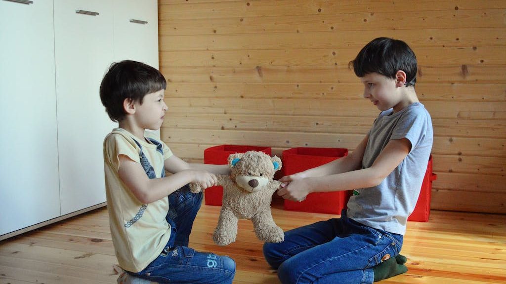 Side view full length irritated fighting brothers sitting on floor and pulling teddy bear to sides. parenting children with sensory needs.